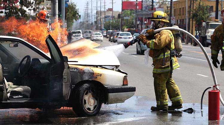 Fireman spraying water under the hood of a car on fire.