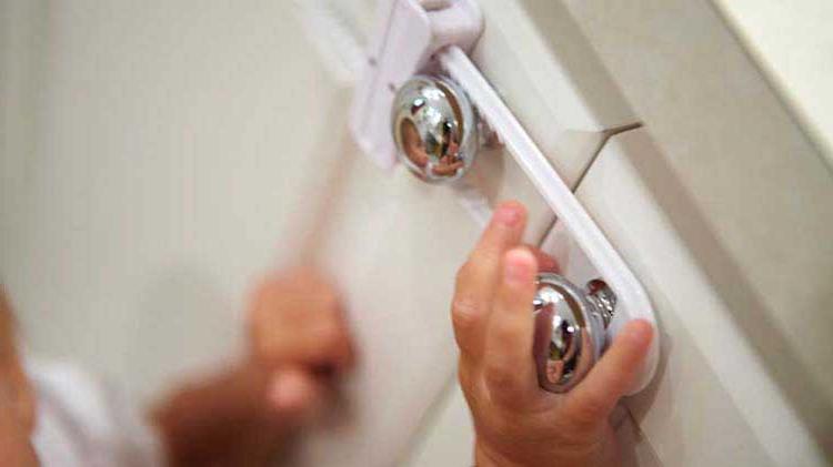 Child's hand on cabinet knob with a safety latch.