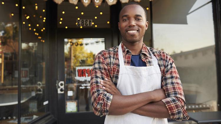 An African American man stands in front of his small business.