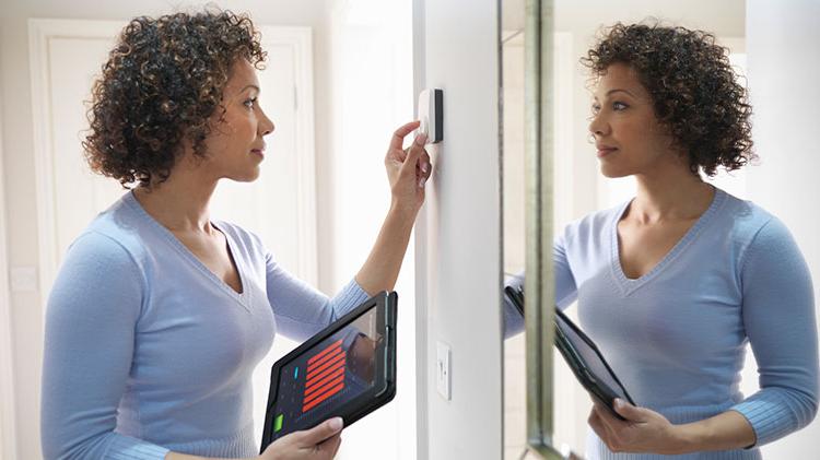 Woman setting her thermostat with a tablet in her other hand.