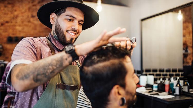 Smiling barber cutting customer's hair in salon.