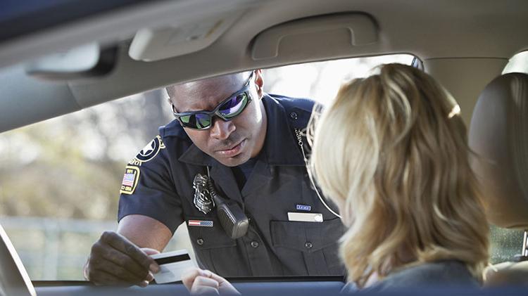 A young woman is pulled over in her car and a police man is talking to her as she hands him her drivers license.