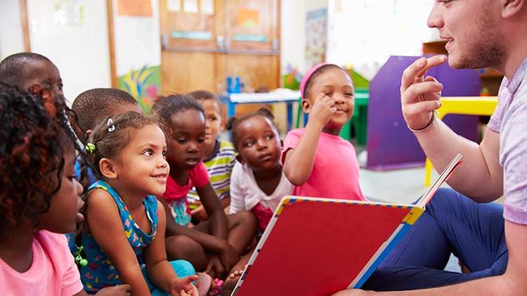 A man is volunteering in a classroom and reading to children.