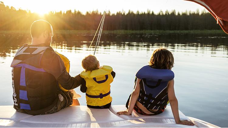 Father and two children fishing off their boat on a sunny lake.